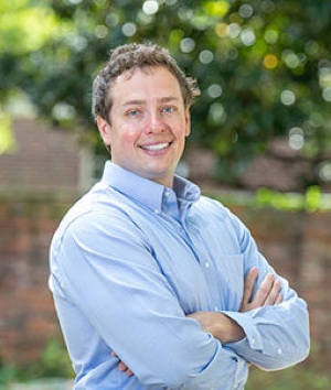 Sam McQuillin, smiling with arms crossed, wearing a light blue button-down shirt, photographed outdoors.