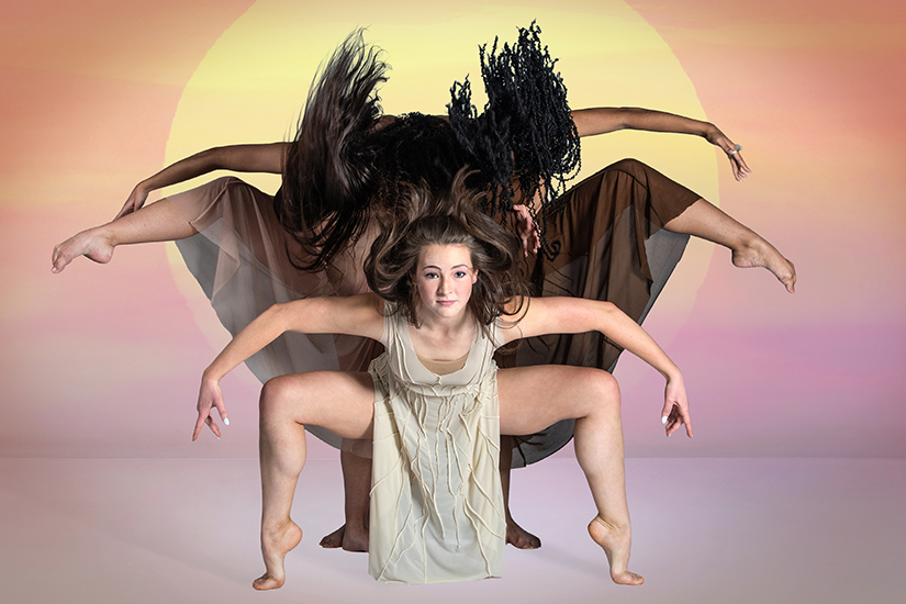 Three female dancers pose against a background showing a bright yellow sun in an orange and purple sky.