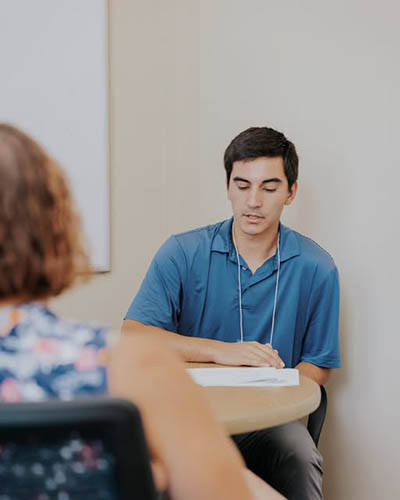 Student sitting at a desk, teacher in foreground viewed from behind.