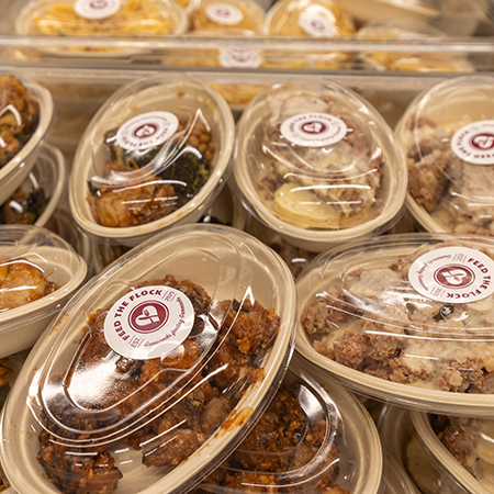 Stacked clear takeout containers filled with prepared meals labeled “Feed the Flock,” highlighting packaged food ready for community distribution through the University of South Carolina hospitality program.