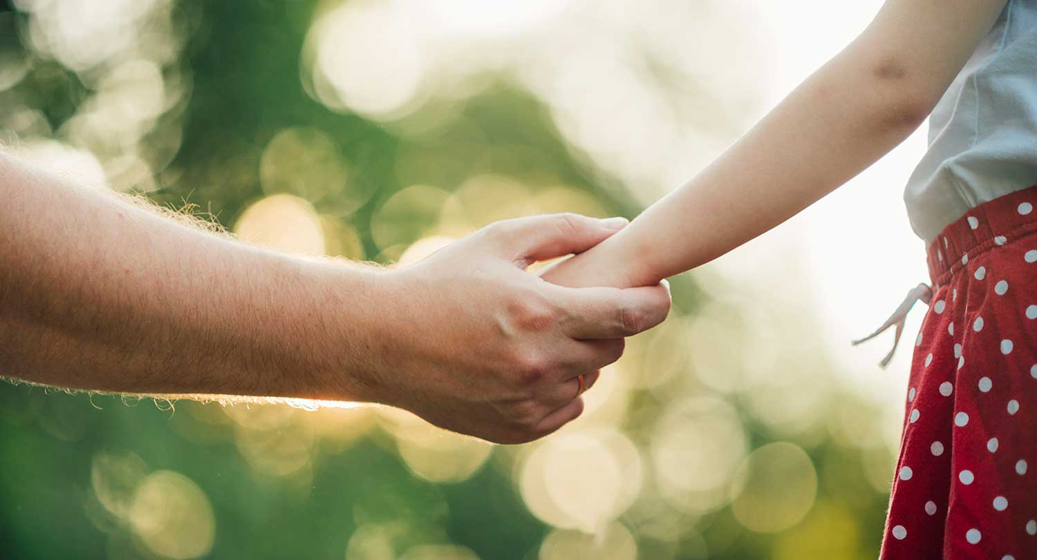 Parent reaches out hand to hold daughter's hand.