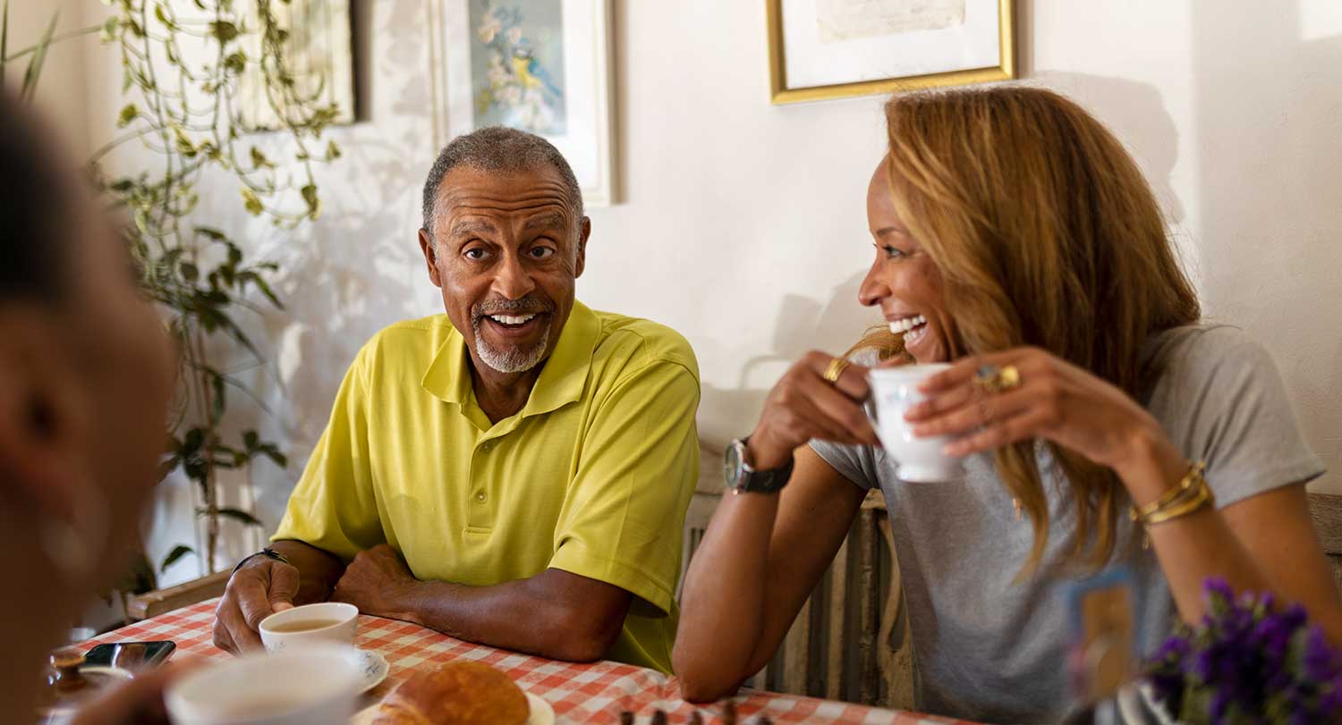 Older male drinking coffee sits next to younger female.