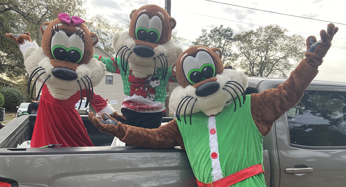 An adult and two children wearing Olly the Otter mascot costumes pose for a picture.